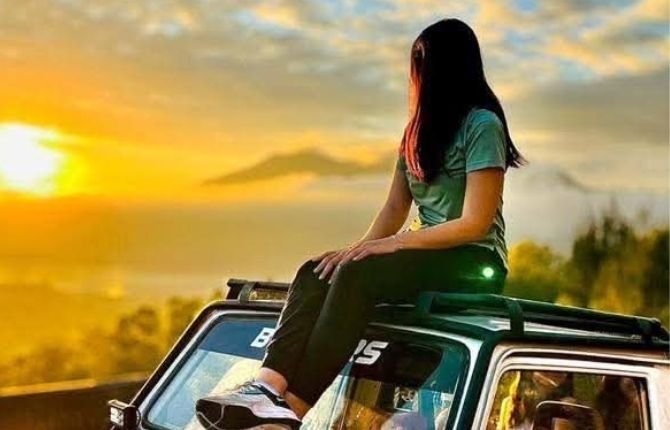 Traveller sitting on top of a jeep watching the sunrise over Mount Batur